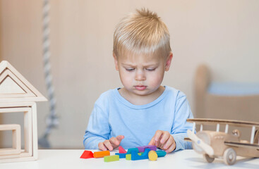 A little boy of 2 years old is playing a developing logistics constructor. Children's wooden toys. Montessori for child development.