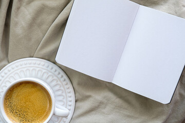 vista superior de xícara de café e página em branco aberto sobre a cama desarrumada sem ninguém e com espaço livre para texto