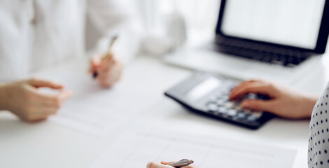 Two accountants using a calculator and laptop computer for counting taxes at white desk in office....
