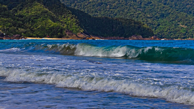 Wave breaking in the blue sea of ​​Trindade, in the background the slopes of the Serra do Mar, covered by the Atlantic forest.
