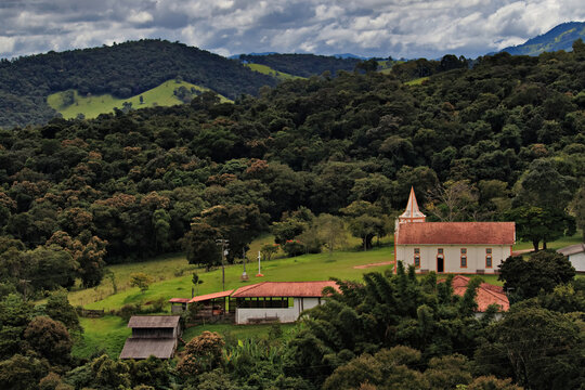 Saint Joseph of Boa Vista church  among lush green mountains, under a dramatic sky.