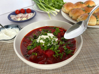 A hearty bowl of traditional Ukrainian borscht topped with fresh herbs and a dollop of sour cream. The vibrant red soup is surrounded by a spread of complementary ingredients.