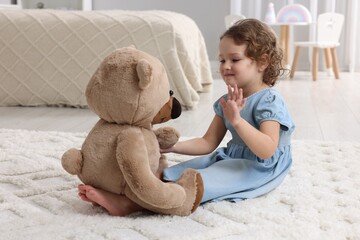 Cute little girl playing with teddy bear on floor at home