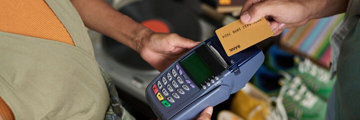 Long exposure of hands of female shop assistant and male consumer during contactless payment with credit card for purchase