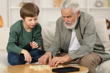 Grandpa and his grandson playing dominoes at table indoors