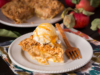 Slice of apple crumb pie topped with a scoop of vanilla ice cream surrounded by fresh picked apples