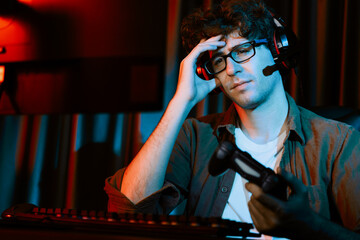 Stressful young gaming streamer team playing with joystick of Esport online on computer fighting harder lost game with to try winner on strategy plan for next at rad neon lighting modern room. Gusher.