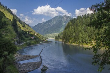A breathtaking natural landscape unfolds showcasing rolling green hills under a vibrant blue sky A serene river meanders through flanked by wildflowers, while distant mountains add a majestic backdrop