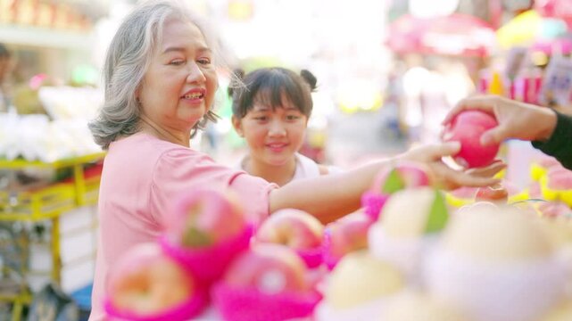 4K Happy Asian family grandmother and little grandchild girl enjoy and fun outdoor lifestyle shopping, choosing and buying fresh fruit during travel city street market on summer holiday vacation.