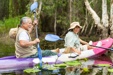 Happy Asian family senior couple kayaking in the river on summer holiday vacation. Healthy elderly people enjoy and fun outdoor active lifestyle travel nature, sport and rowing a boat in the lake.