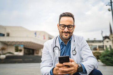 Adult man doctor sit and use cellphone while hold clipboard outdoor