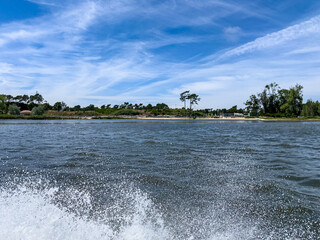 A view of the calm riverside river with soft splashes of water against the shore beneath a bright...