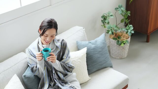 寒い、冬、暖かい、コーヒー、笑顔、女性、日本人、暖冬、対策、防寒、ストール、ショール、ブランケット、コピースペース、インテリア、リビングルーム、ライフスタイル、おしゃれ、リラックス、ほっこり、安心、ソファー、若い、寒暖差、紅茶、カップ、飲む、暖房、エアコン、マフラー、ポジティブ、快適、節電、室内、明るい、省エネ、爽やか、毛布、シンプル、キレイめ、きれいめ、セーター、ニット、寒さ、寒気、冷気、住宅、