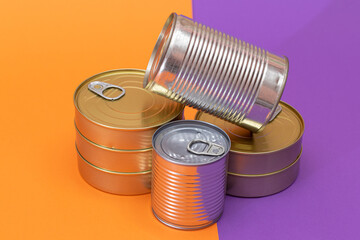 A Group of Stacked Tin Cans with Blank Edges on Split Orange and Violet Background. Canned Food. Different Aluminum Cans for Safe and Long Term Storage of Food. Steel Sealed Food Storage Containers