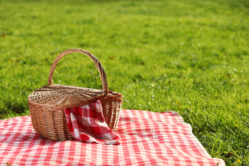 One picnic wicker basket with checkered napkin and blanket on green grass. Space for text