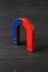 One horseshoe magnet on black wooden table, closeup