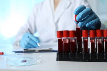 Laboratory testing. Doctor taking test tube with blood sample while working at table indoors,...