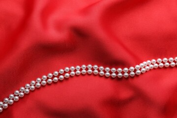 Beautiful pearl necklace on red cloth, top view