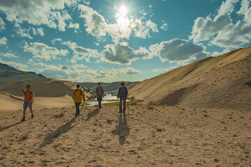 Obraz premium A group of friends on the background of the sand of the sky and the river on the slope. The travelers are walking towards the camera. Tourists walk along the sand against the background of the sky and