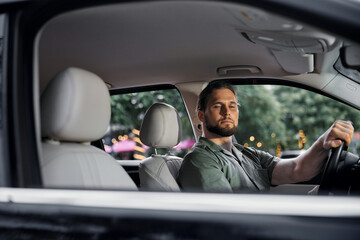 A young man in a car looking relaxed while driving in a city environment