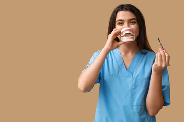 Female dentist with jaw model and tool on brown background. World Dentist Day