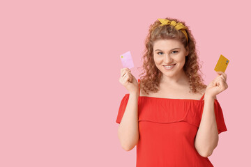 Beautiful young woman with credit cards on pink background