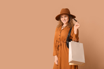 Beautiful young woman with credit card and shopping bags on brown background