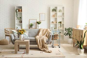 Sofa with cushions, plaid and wild flowers in vase on coffee table in living room