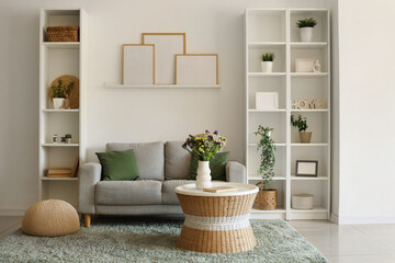 Cozy sofa and vase with wild flowers on coffee table in living room