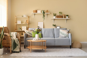 Comfortable sofa, armchair and wild flowers in vase on coffee table in living room