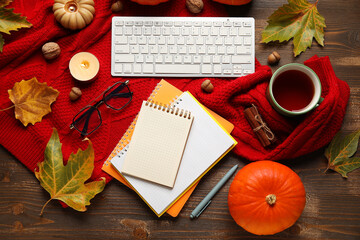 Notebooks with computer keyboard, tea cup, sweater and autumn decor on wooden background