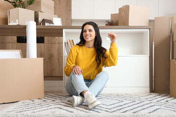 Beautiful woman with key from new flat sitting in kitchen on moving day