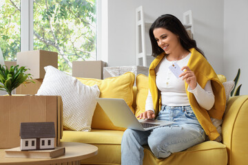 Beautiful woman with credit card using laptop in room on moving day