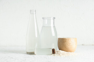 Bottles of natural rice water and bowl with grains on light background