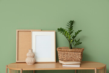 Frames, vase and houseplant on shelving unit near green wall in room. Closeup