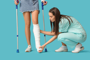 Young woman with broken leg and doctor on blue background