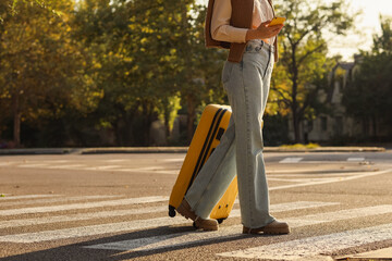 Woman with suitcase and mobile phone crossing road. Autumn travelling