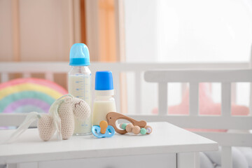 Bottles of baby milk formula, toys and pacifier on table in children's room