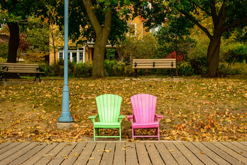 Two colorful beach chairs on a wooden boardwalk in fall with a background of trees and fallen leaves shot at Balmy Beach in Toronto's Beaches neighbourhood