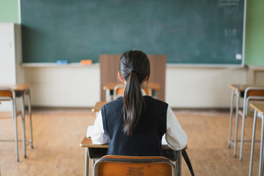 教室で座っている日本人の女子中学生の後ろ姿