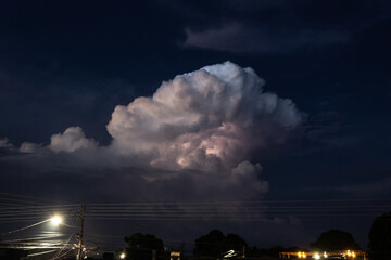 Lightning strike in the night sky with clouds and electricity pole.