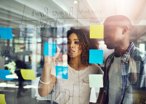 Business people, writing and schedule planning with vision with glass board for brainstorming at office. Businessman, woman or employees taking notes for meeting, project or reminder at workplace