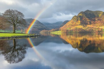 A serene landscape featuring a rainbow over a calm lake, surrounded by mountains and trees.