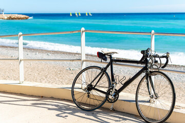A bicycle sits parked along a ramp to the beach along Promenade du Soleil as a group of sailboats are blurred in the distance on the French Riviera in Menton, France