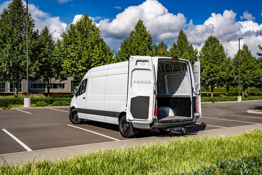 Commercial compact white mini van make delivery to the customer standing with open back doors on the parking lot for a cargo unload