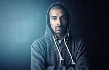 Man, arms crossed and earphones in studio for workout with portrait, training and hoodie by dark background. Person, audio and streaming music to start exercise, pride and fitness routine in Mexico