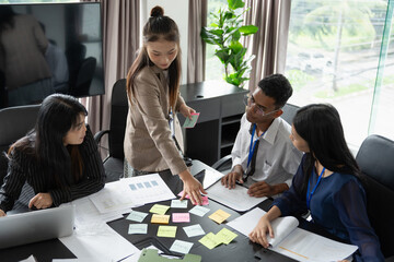 Group of Asian people using sticky notes on meeting table, brainstorming idea in modern office