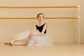 Fototapeta premium A ballet dancer sits on the floor in a dance studio, demonstrating elegance and poise