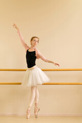 A ballet dancer performs an elegant stretch on pointe, with arms raised while holding the barre for...