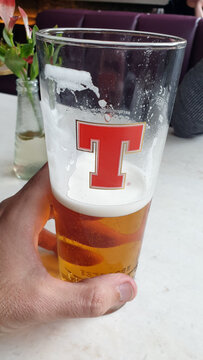Closeup of hand holding a pint glass half full or half empty of Tennent's Lager drinking alcohol in Glasgow, Scotland UK - taken on 2nd April 2024 
